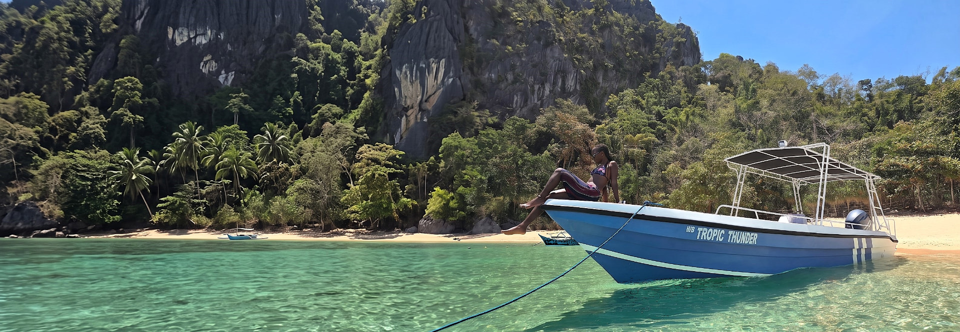 Guest relaxing on the bow of M/B Tropic Thunder in the turquoise shallows of Bacuit Bay, El Nido