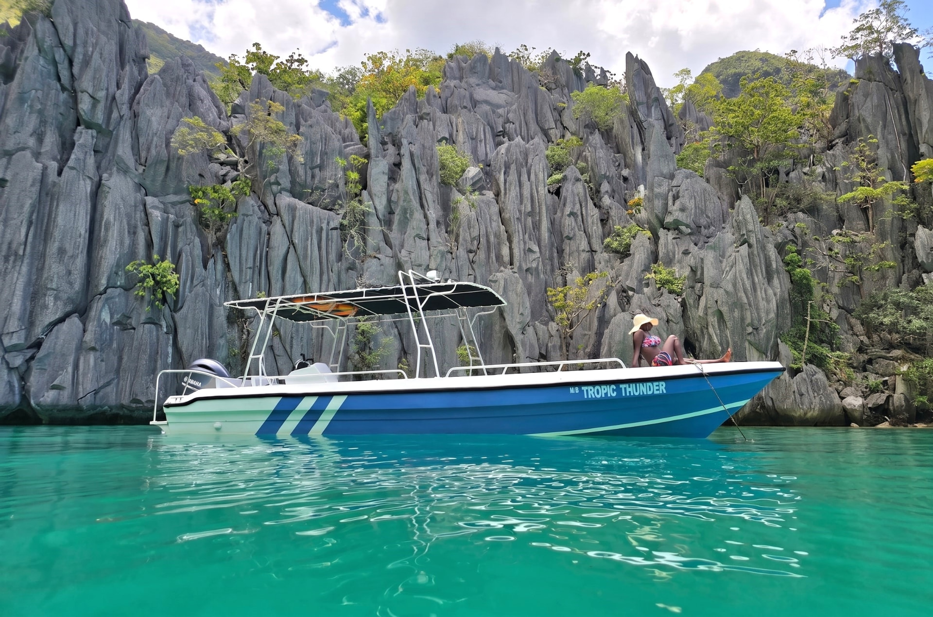 M/B Tropic Thunder anchored in the turquoise water of Cadlao Lagoon with a guest relaxing on the bow